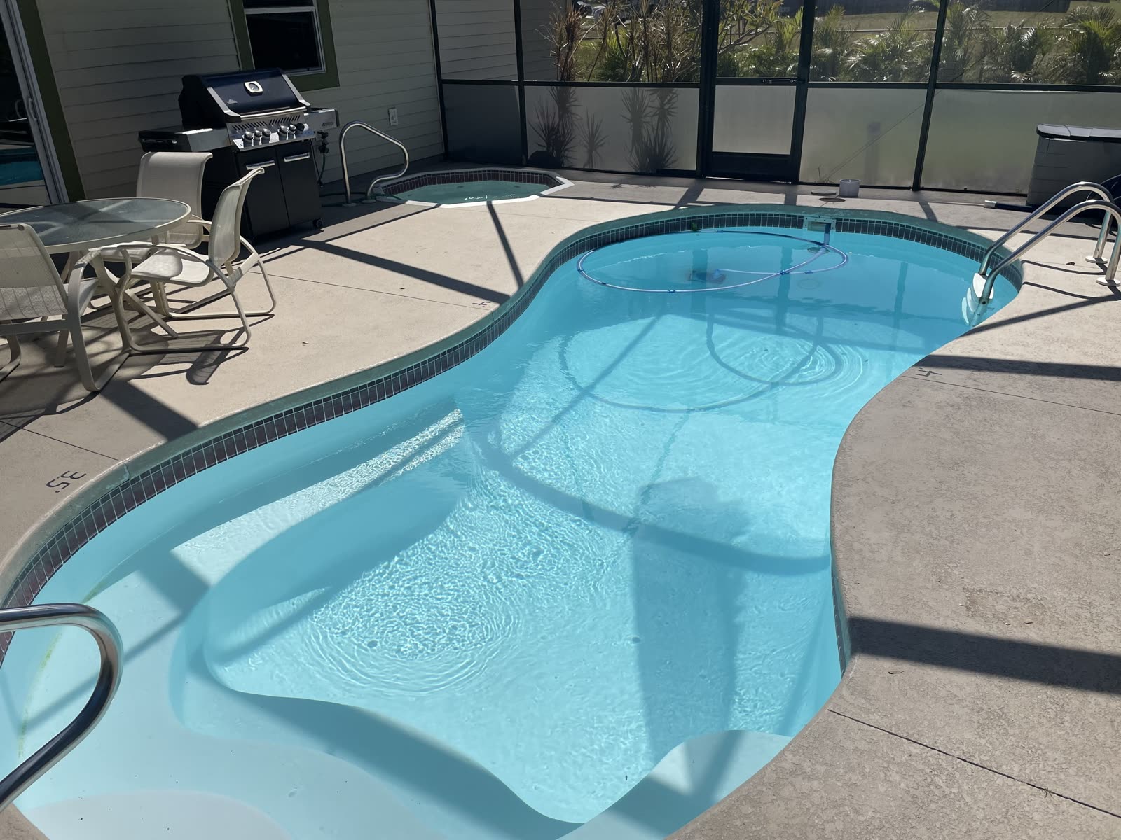 Daytime screened lanai at Sunshine Villa in Cape Coral, with the private kidney-shaped pool, hot tub, dining table, and grill