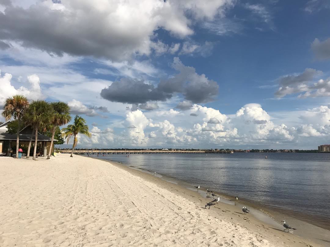 Yacht Club Beach on the Caloosahatchee River in Cape Coral, with sand, palms, and a long pier